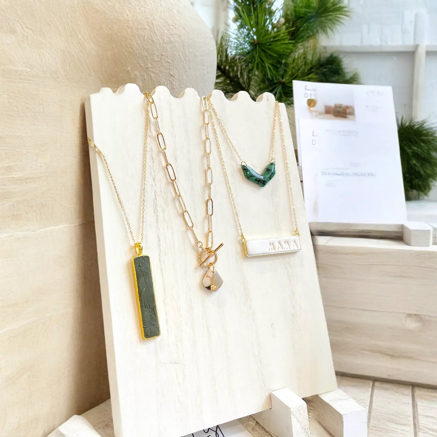 Necklaces displayed on a white stand with a blurred greenery background